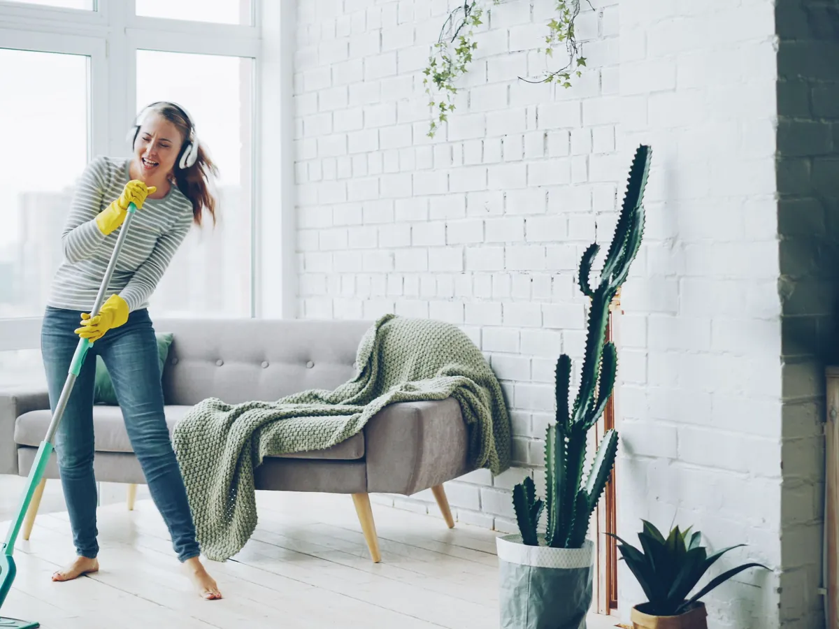 Cheerful cleaner in yellow gloves mopping the floor of a bright living room.