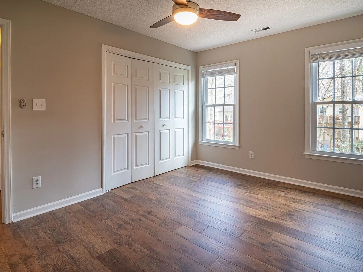 Empty bedroom with wood-look floors, closet doors and daylight from two windows, ready for move-out.